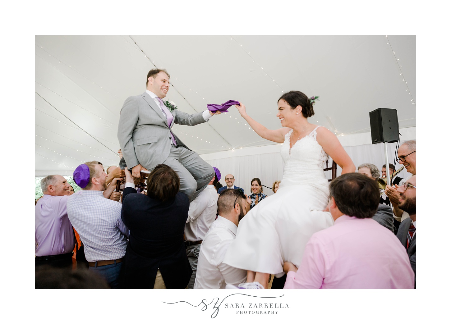bride and groom up in chairs for hora holding purple napkin