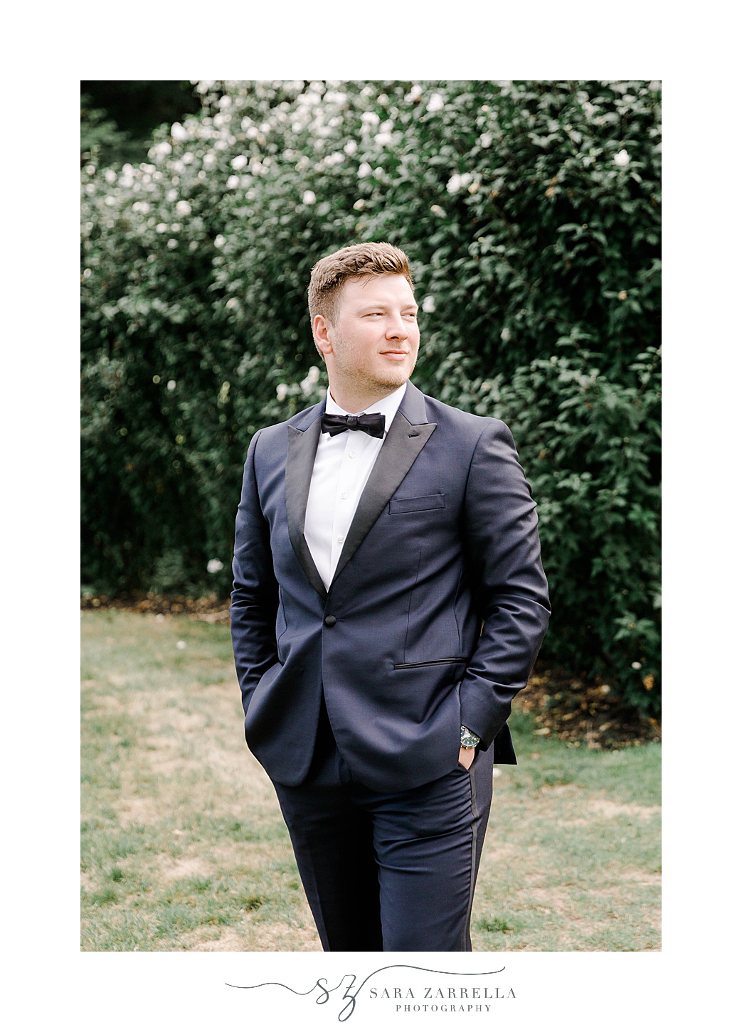 groom stands with hands in pockets in navy suit