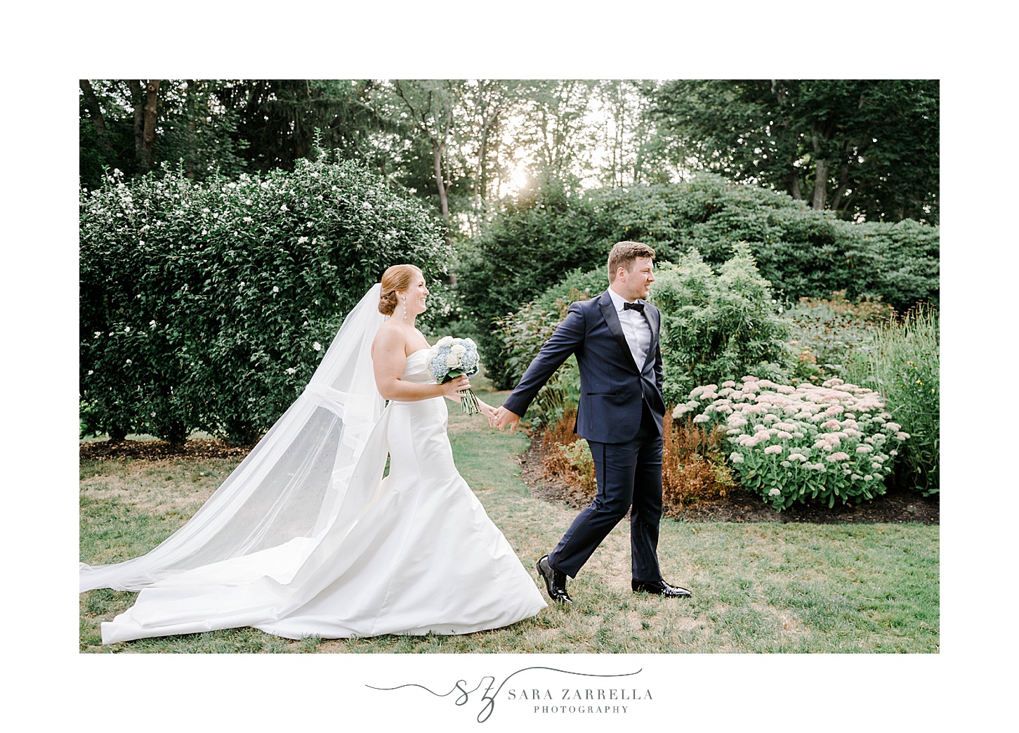 groom in navy suit leads bride in strapless gown through gardens at Glen Manor House
