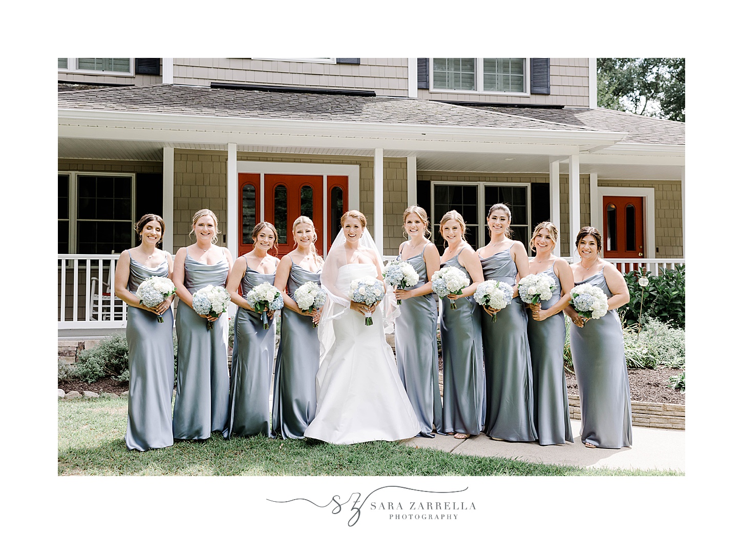 brie poses with bridesmaids in blue dresses in front of RI home
