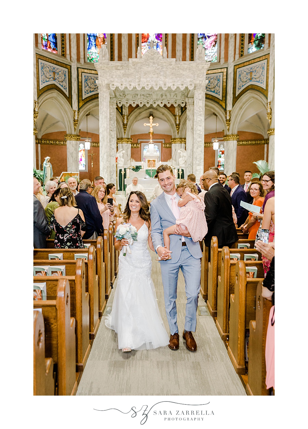 bride and groom walk up aisle with daughter during Catholic wedding ceremony in Newport RI