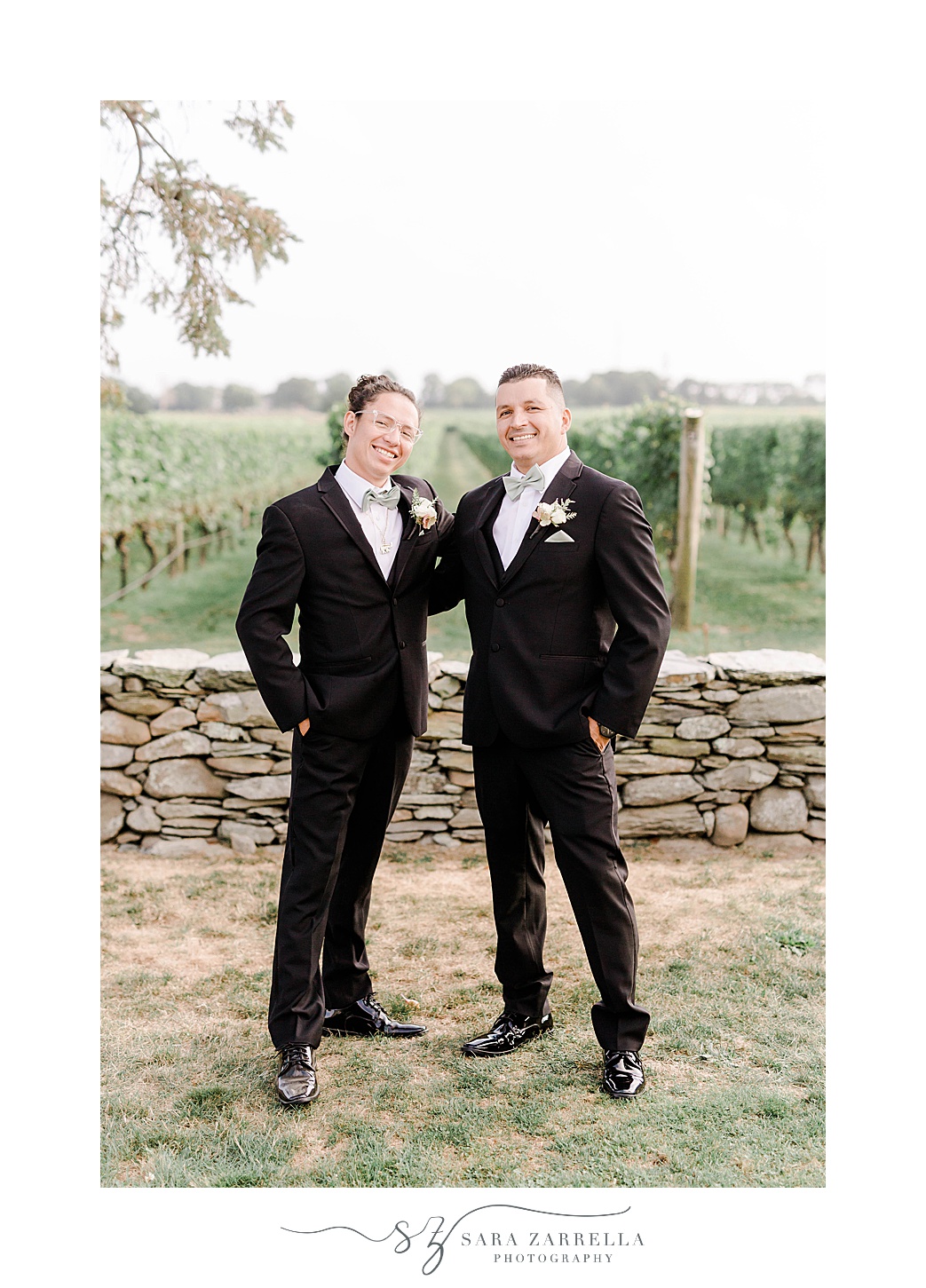 groom poses with brother by stone wall at Newport Vineyards