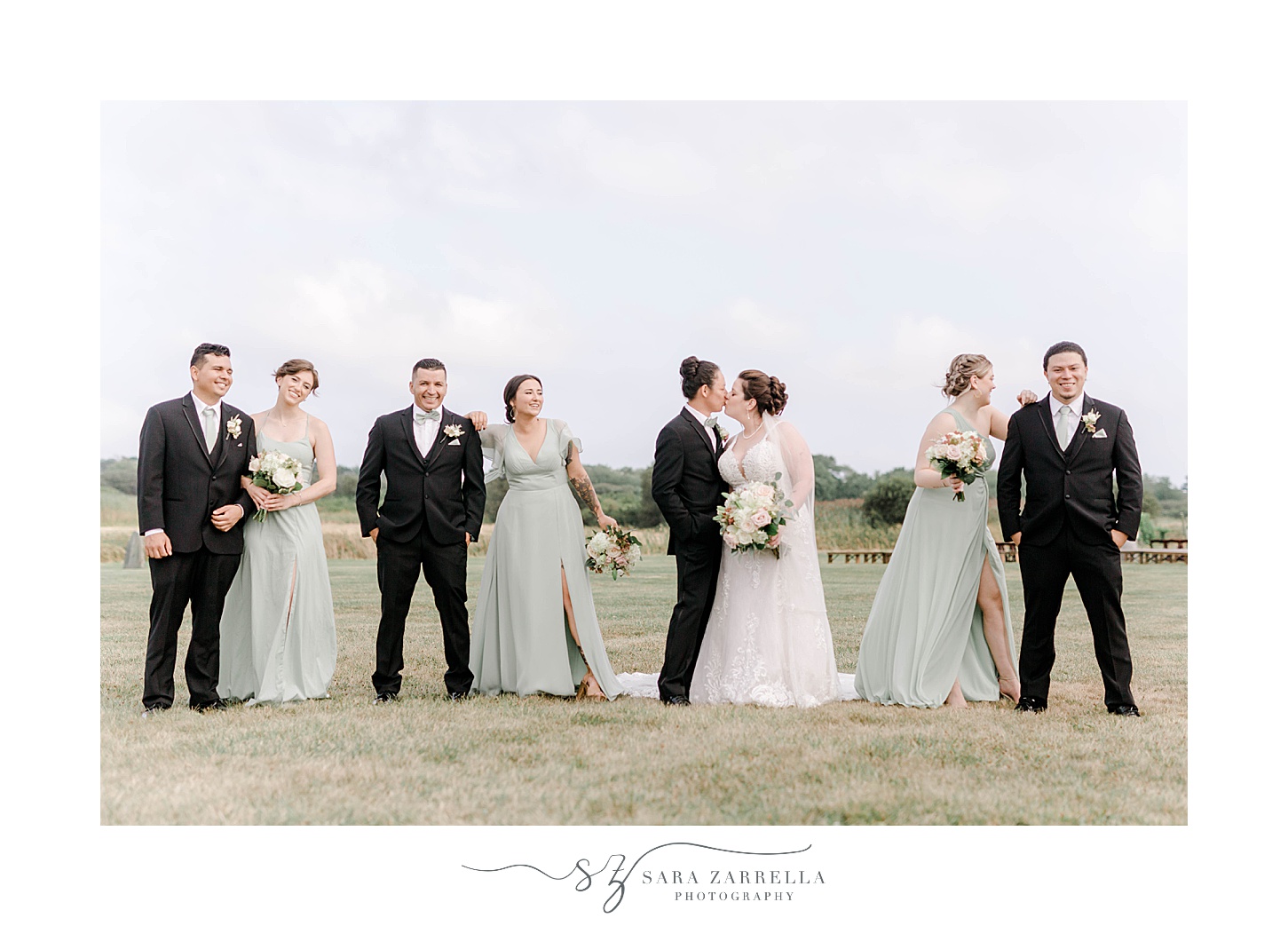 bride and groom kiss with wedding party around them