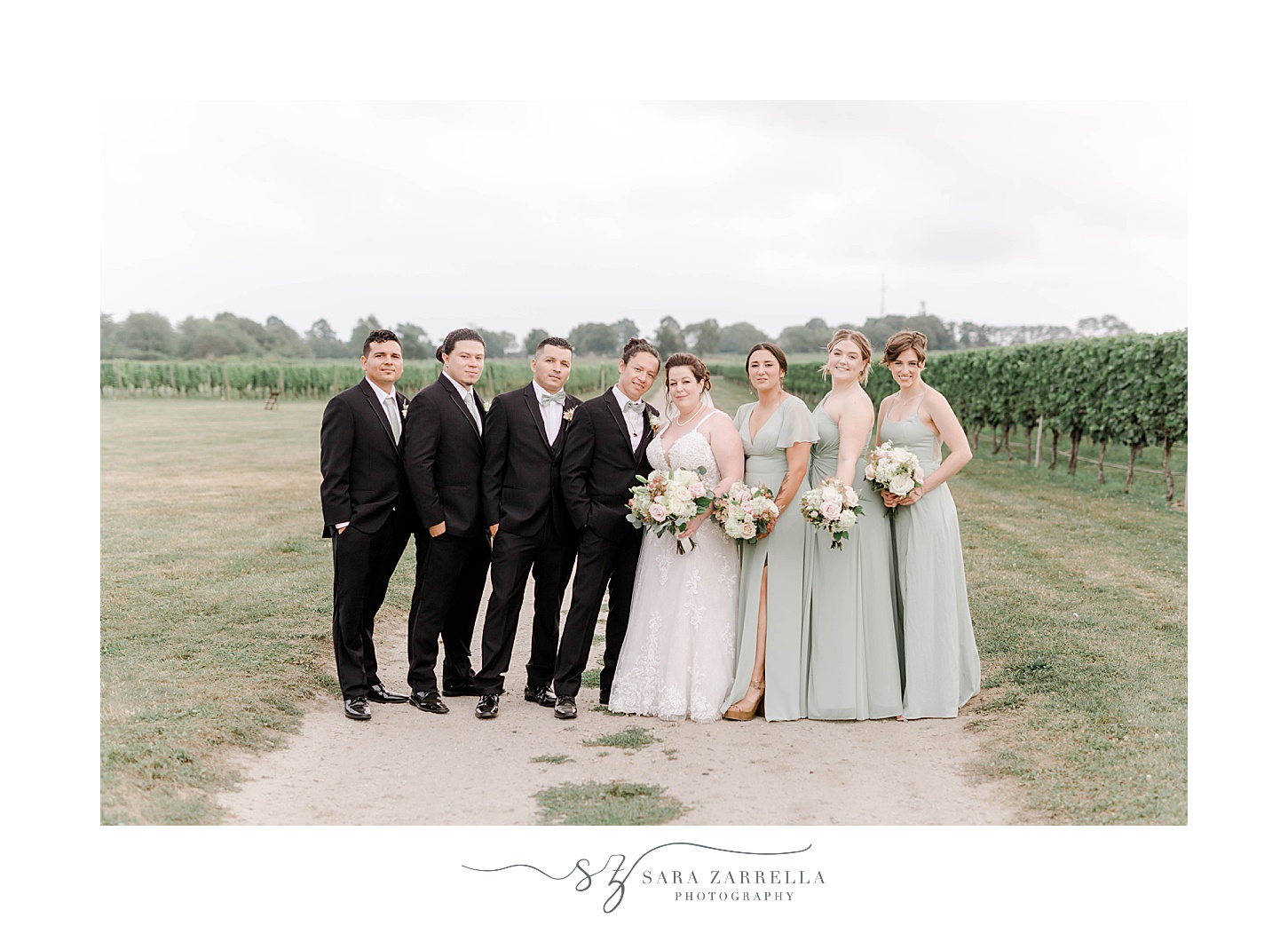 newlyweds stand with bridal party on either side of them on path at Newport Vineyards