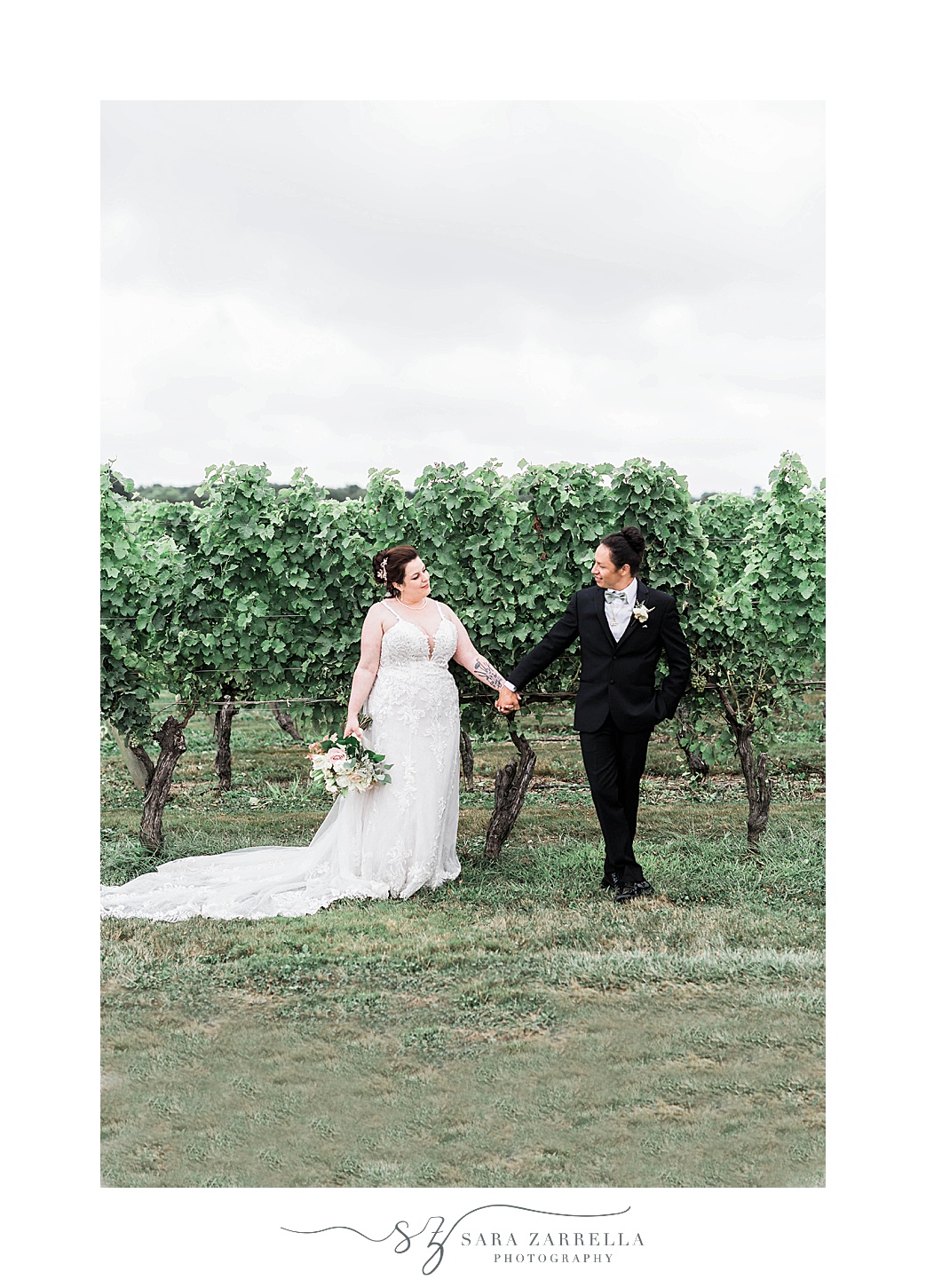 bride and groom hold hands standing in front of row of grape vines