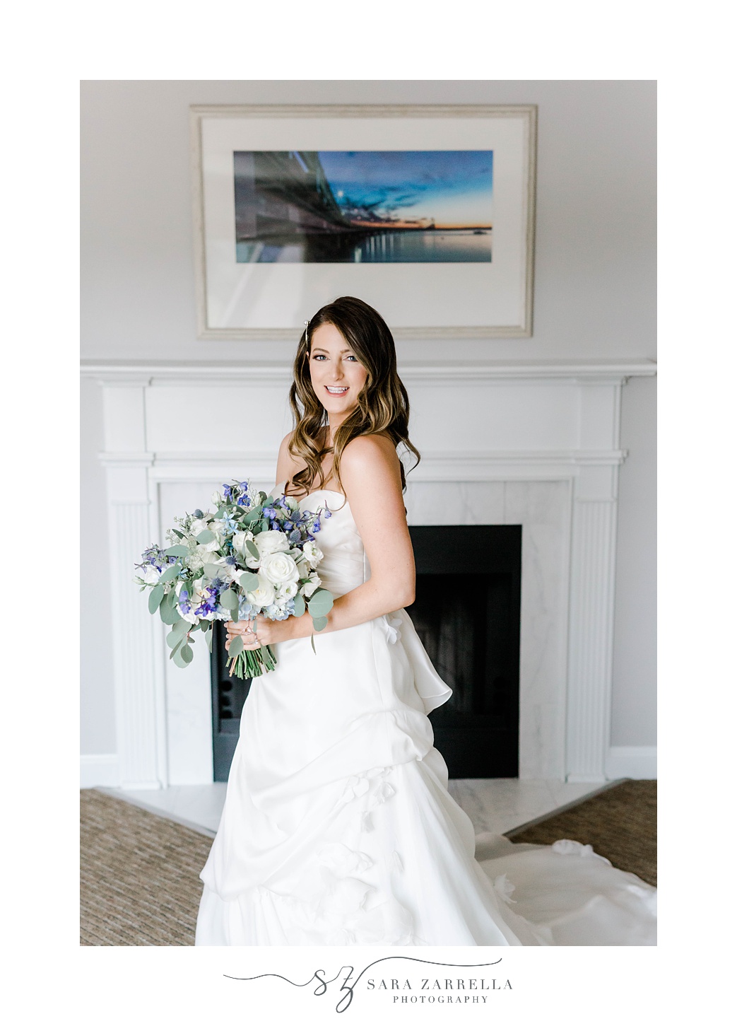 bride poses in front of fireplace in strapless gown with purple and white bouquet 