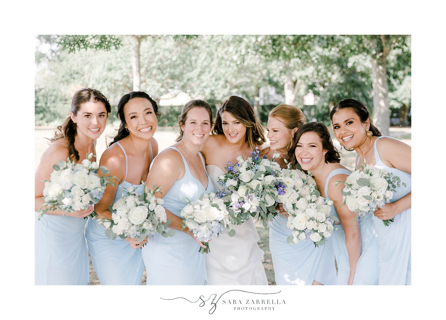 bride and bridesmaids in blue gowns hug in Newport RI park