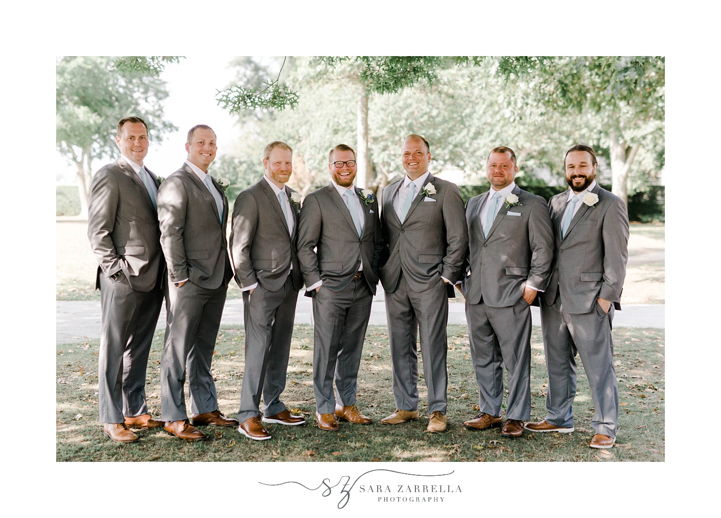 groom and groomsmen in grey suits stand together in park