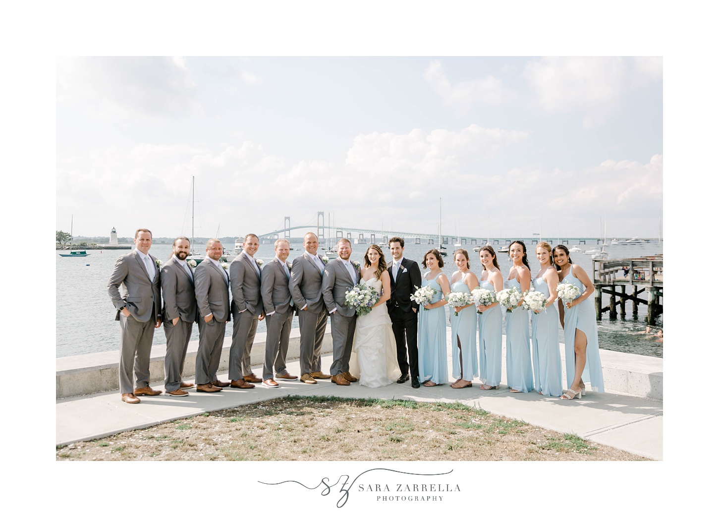 newlyweds stand with bridal party in front of Newport Bridge