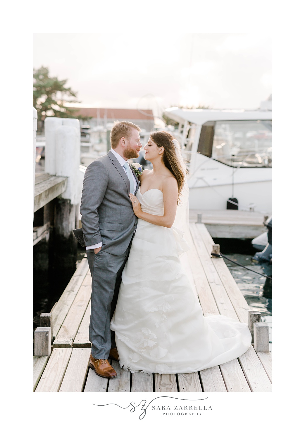 bride hugs groom on dock with boats behind them