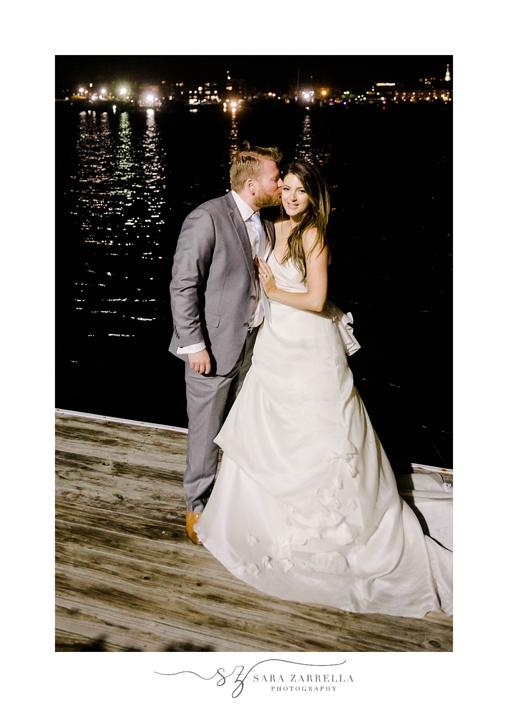 groom kisses bride's forehead during night portraits on dock in Newport RI
