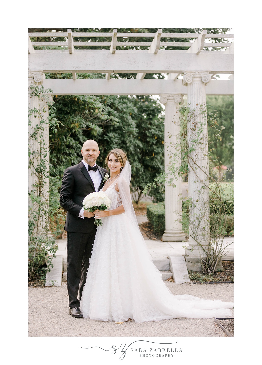 bride and groom smile under stone pillar at Rosecliff Mansion