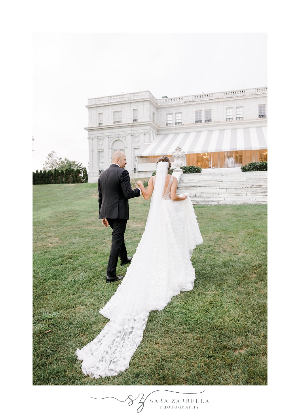 groom helps bride up hill at Rosecliff Mansion