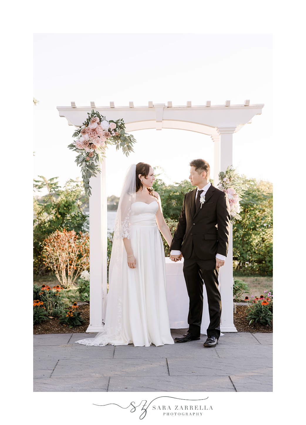 bride and groom stand by white arbor at The Boat House