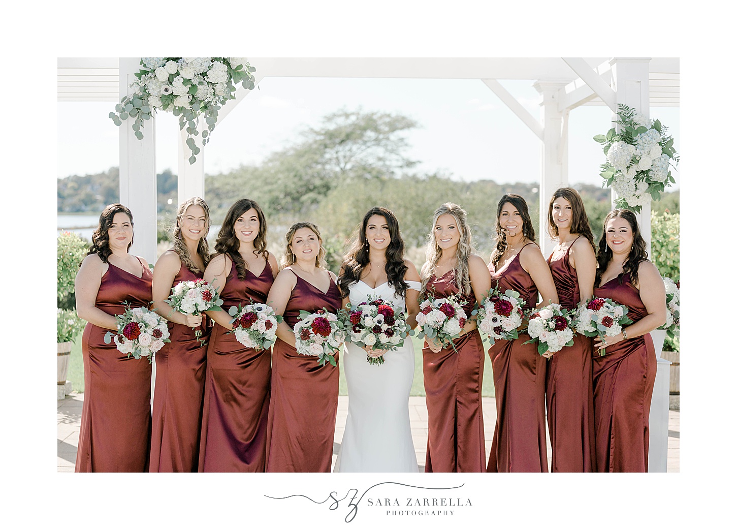 bride stands with bridesmaids in burgundy gowns