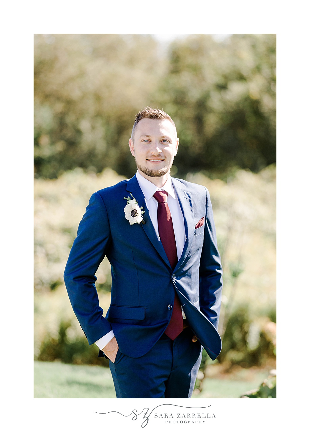 groom stands in navy suit with hands in pockets