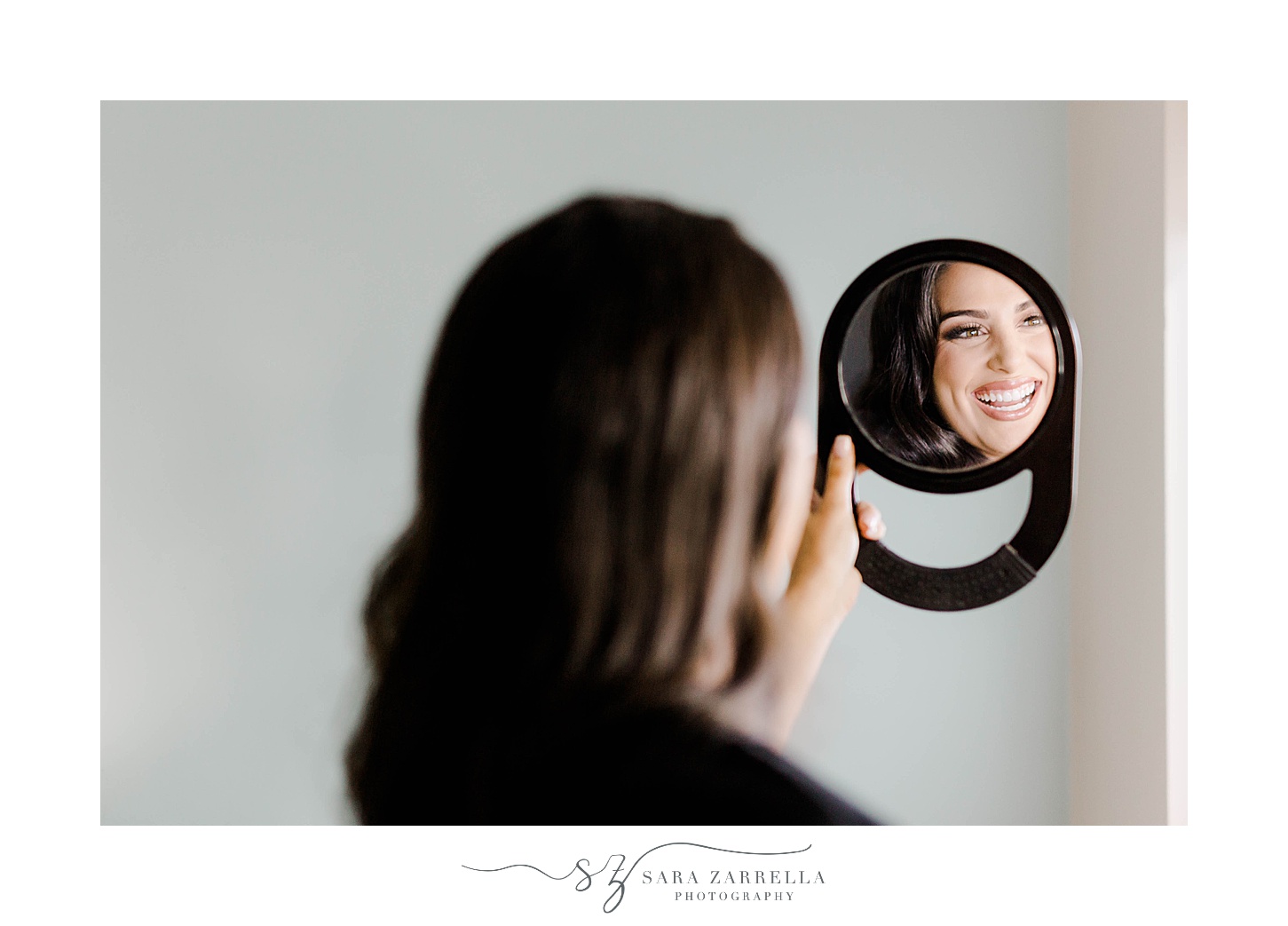 bride smiles looking at makeup in small black mirror
