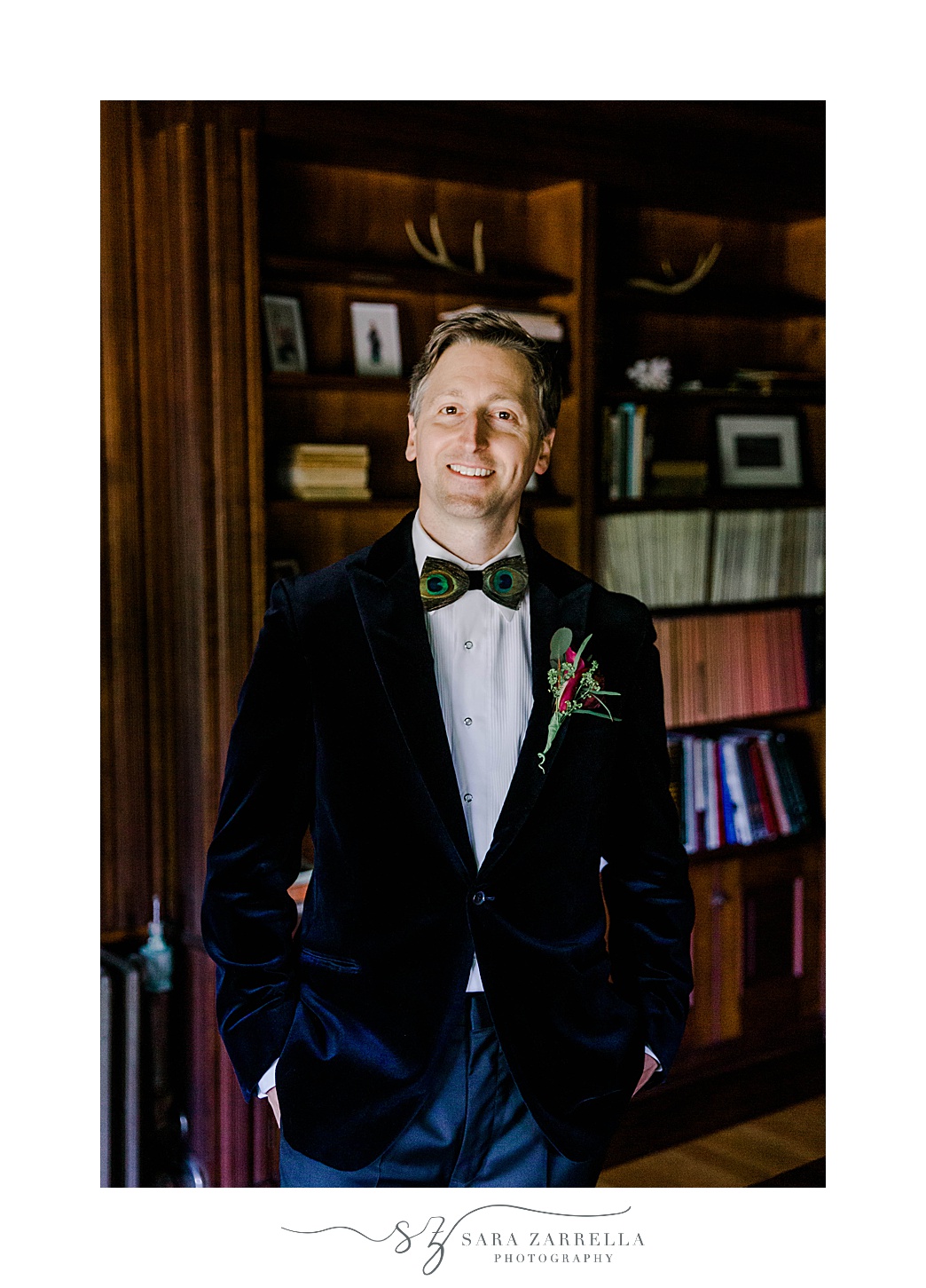 groom in velvet suit jacket smiles in library at Eustis Estate