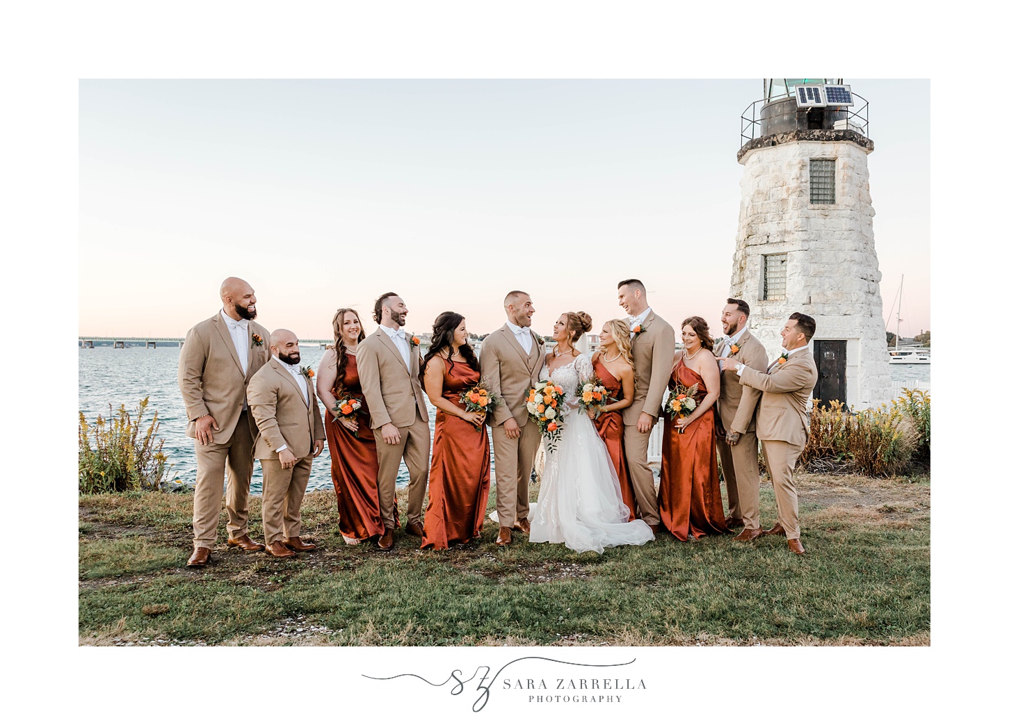 bridesmaids in orange gowns and groomsmen in tan suits walk by Newport Lighthouse 