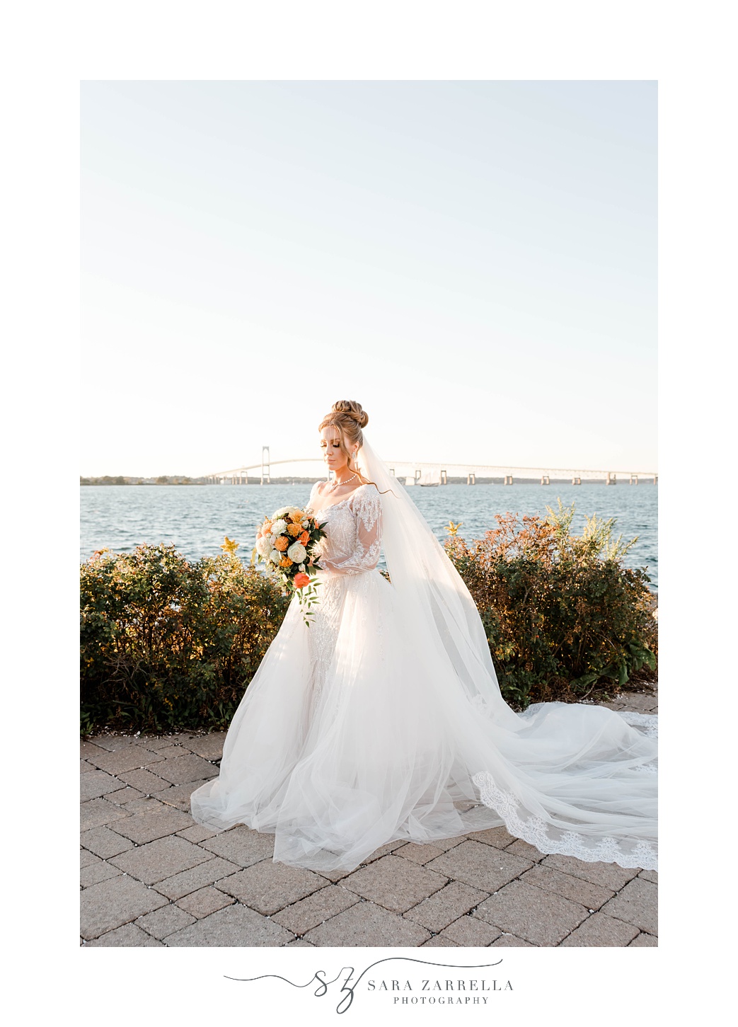 bride stands with veil behind her holding bouquet with orange flowers 
