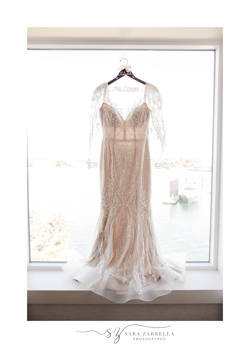bride's wedding dress with lace sleeves hangs in window 