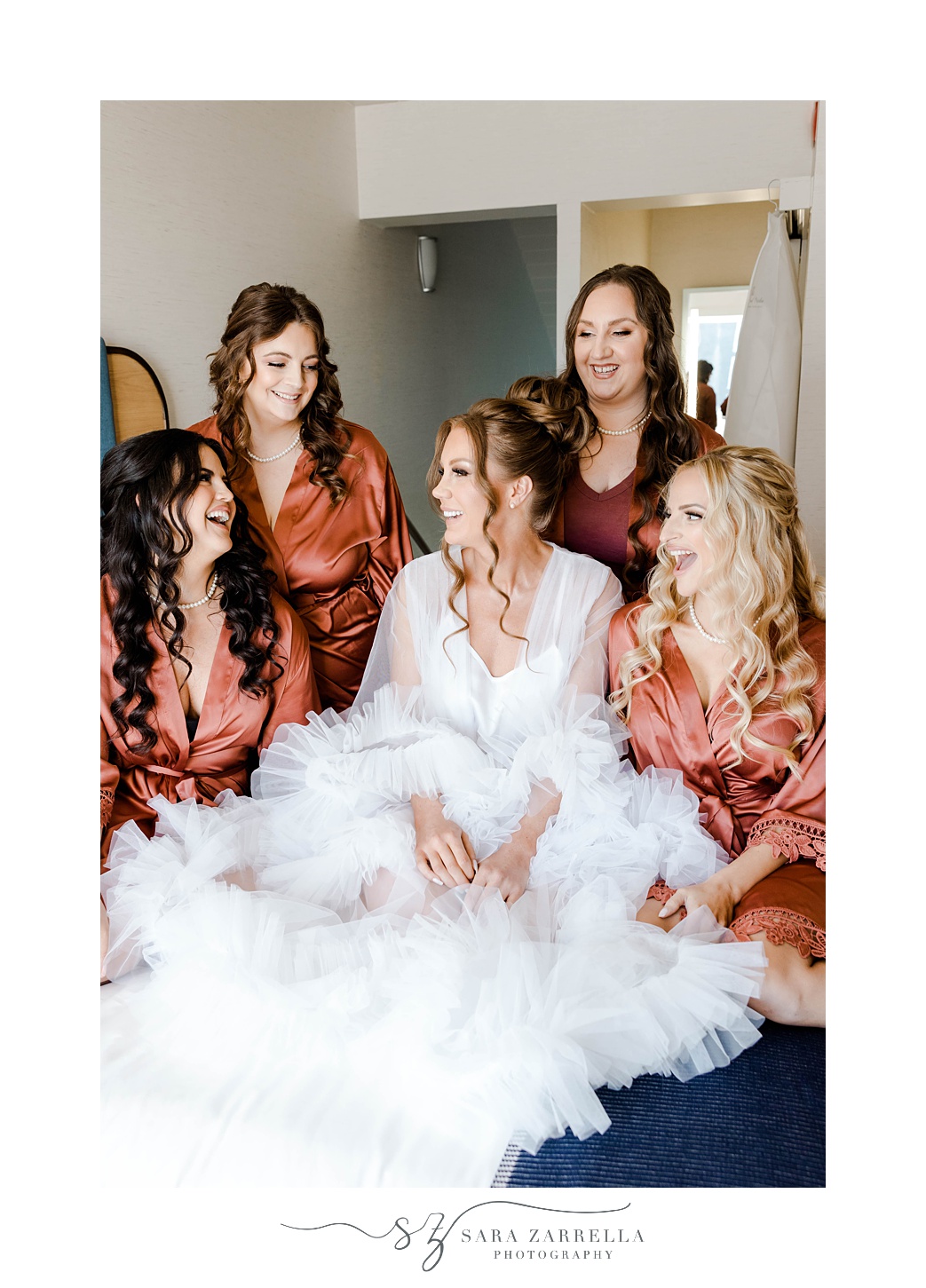 bride laughs with bridesmaids in orange robes 