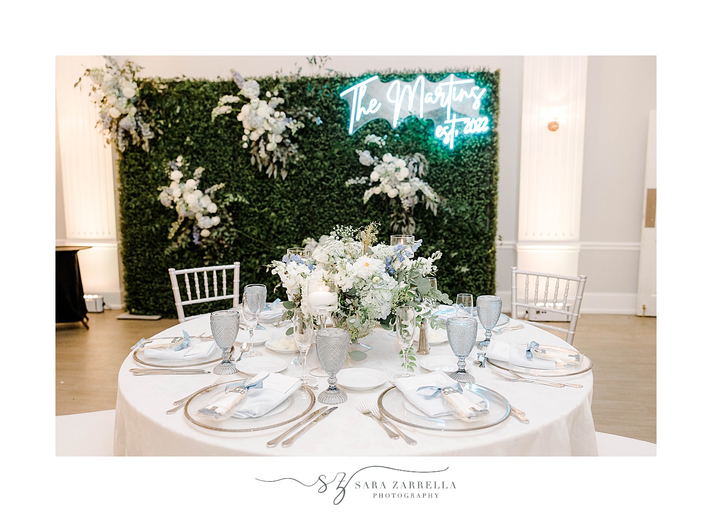sweetheart table in front of greenery wall with neon sign