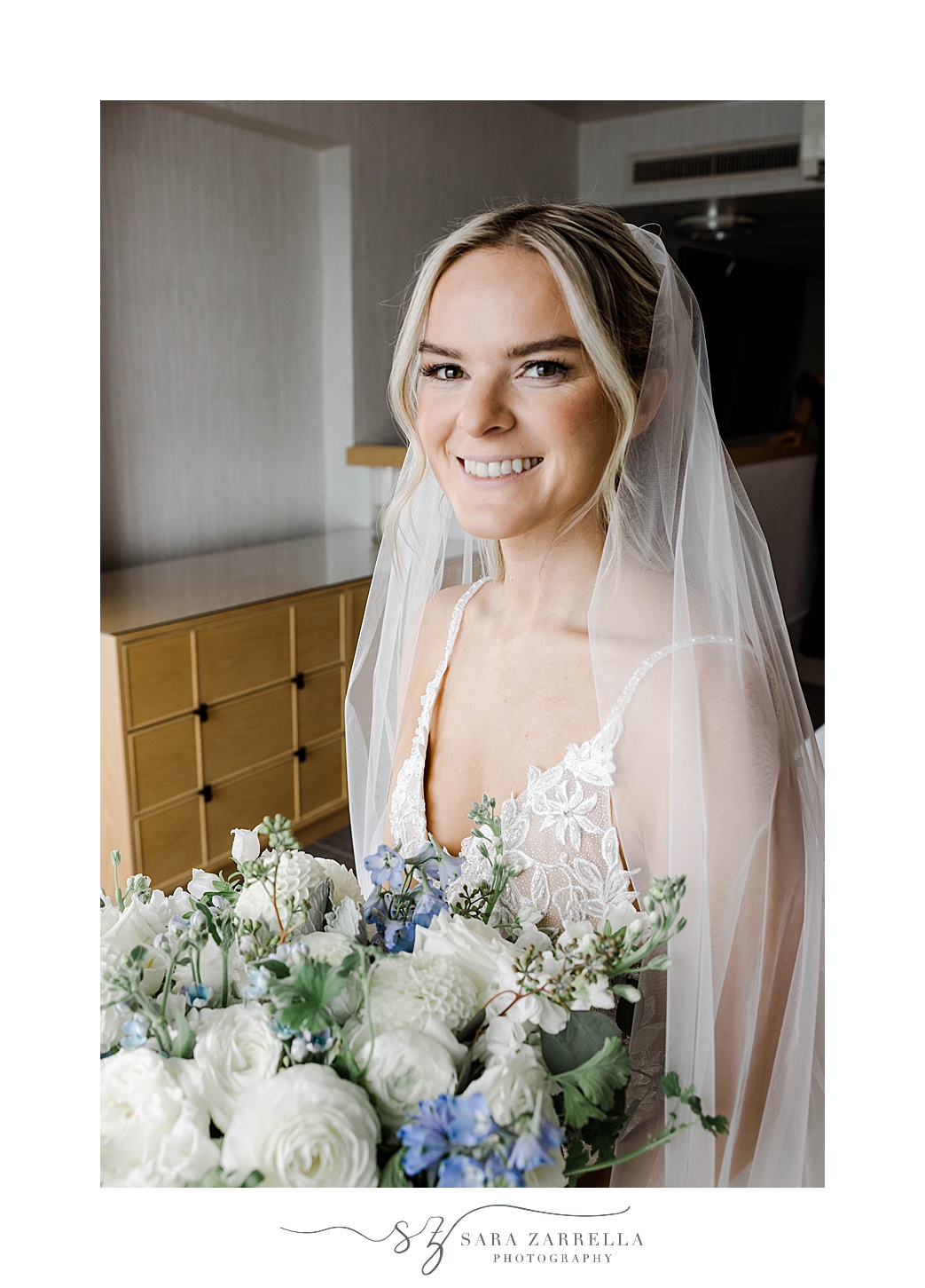 bride smiles with veil behind her with blue and white wedding bouquet 