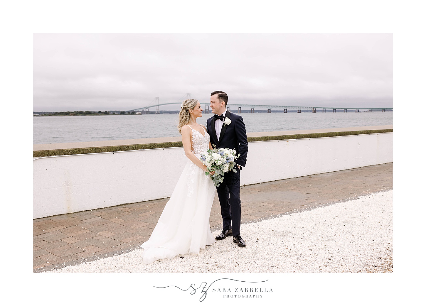 newlyweds pose by waterfront and Newport Bridge 