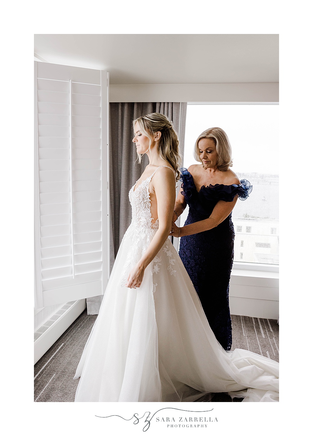 mother in navy gown helps bride into wedding gown