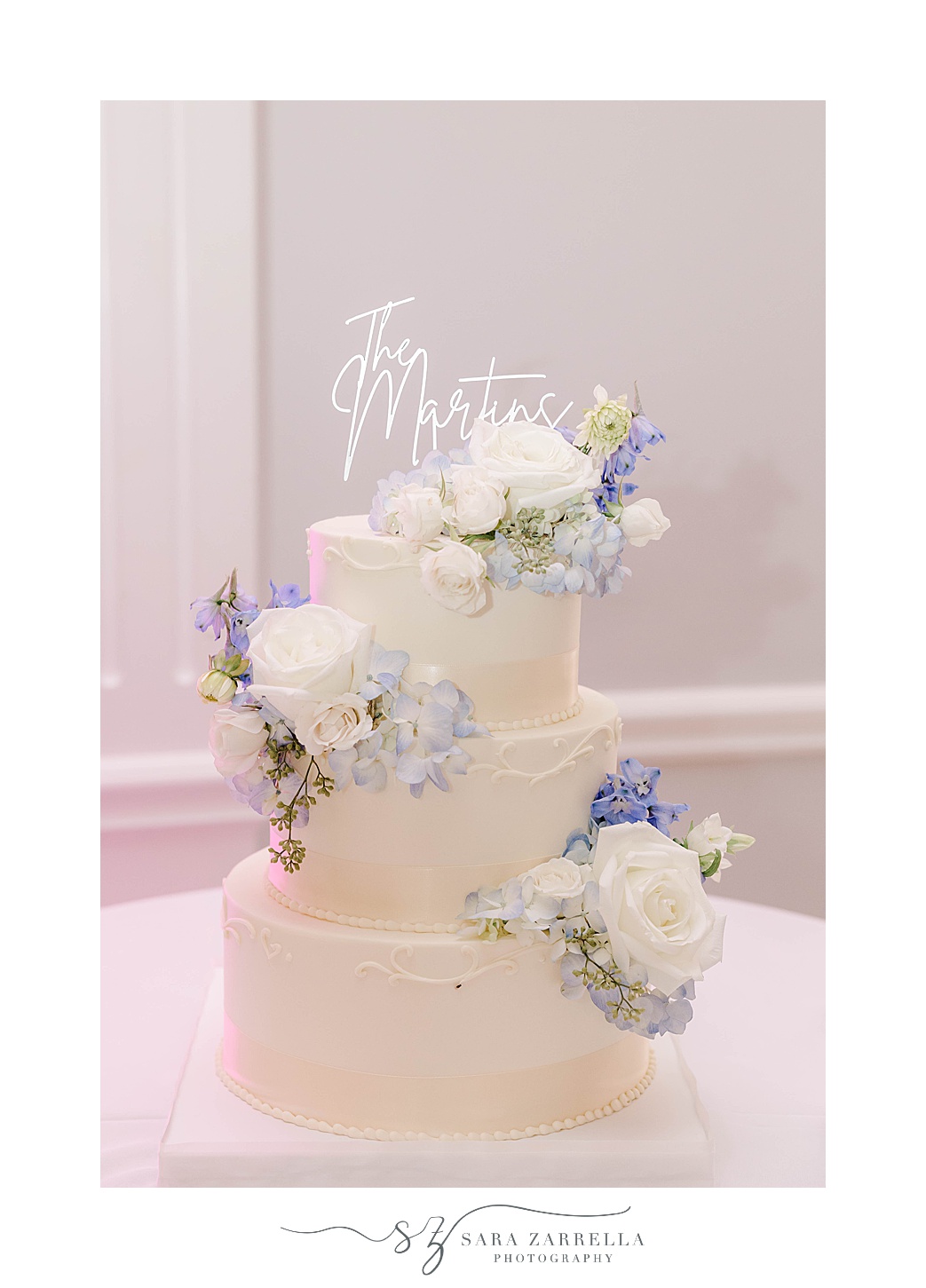 tiered wedding cake with blue and white flowers and custom topper 