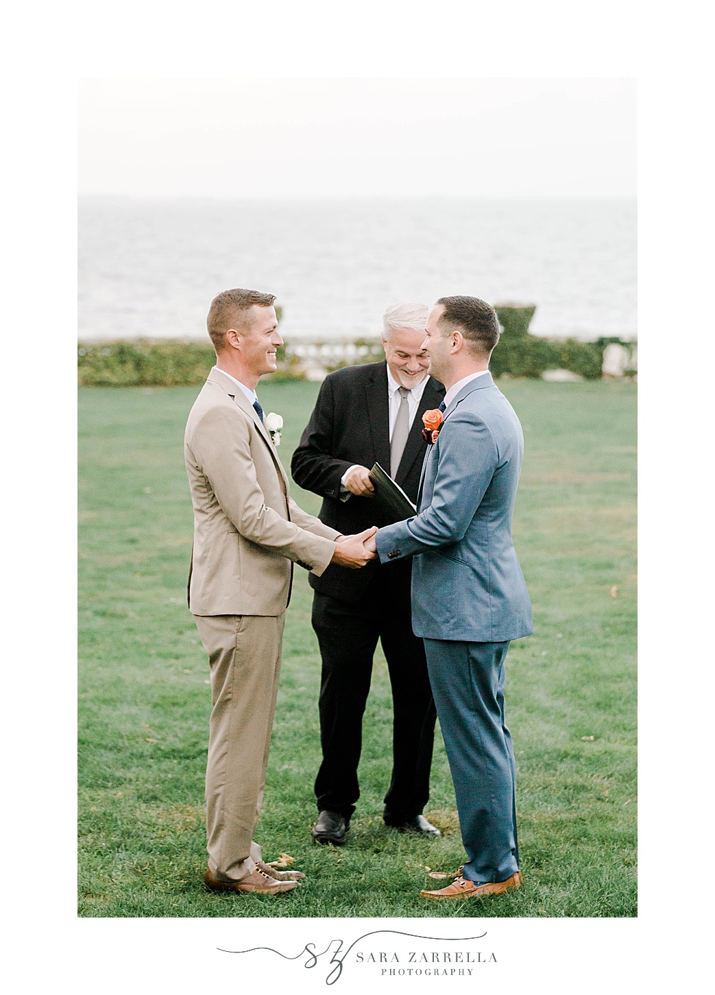 grooms hold hands exchanging vows on lawn at Rosecliff Mansion