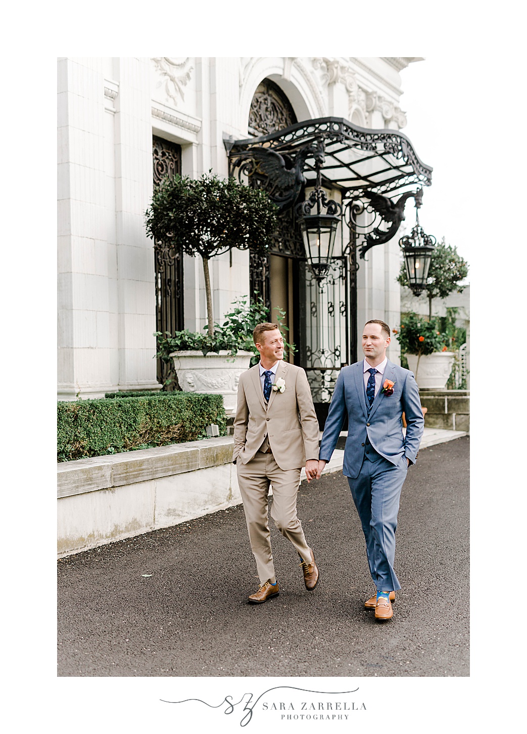 grooms hold hands walking outside the front of Rosecliff Mansion