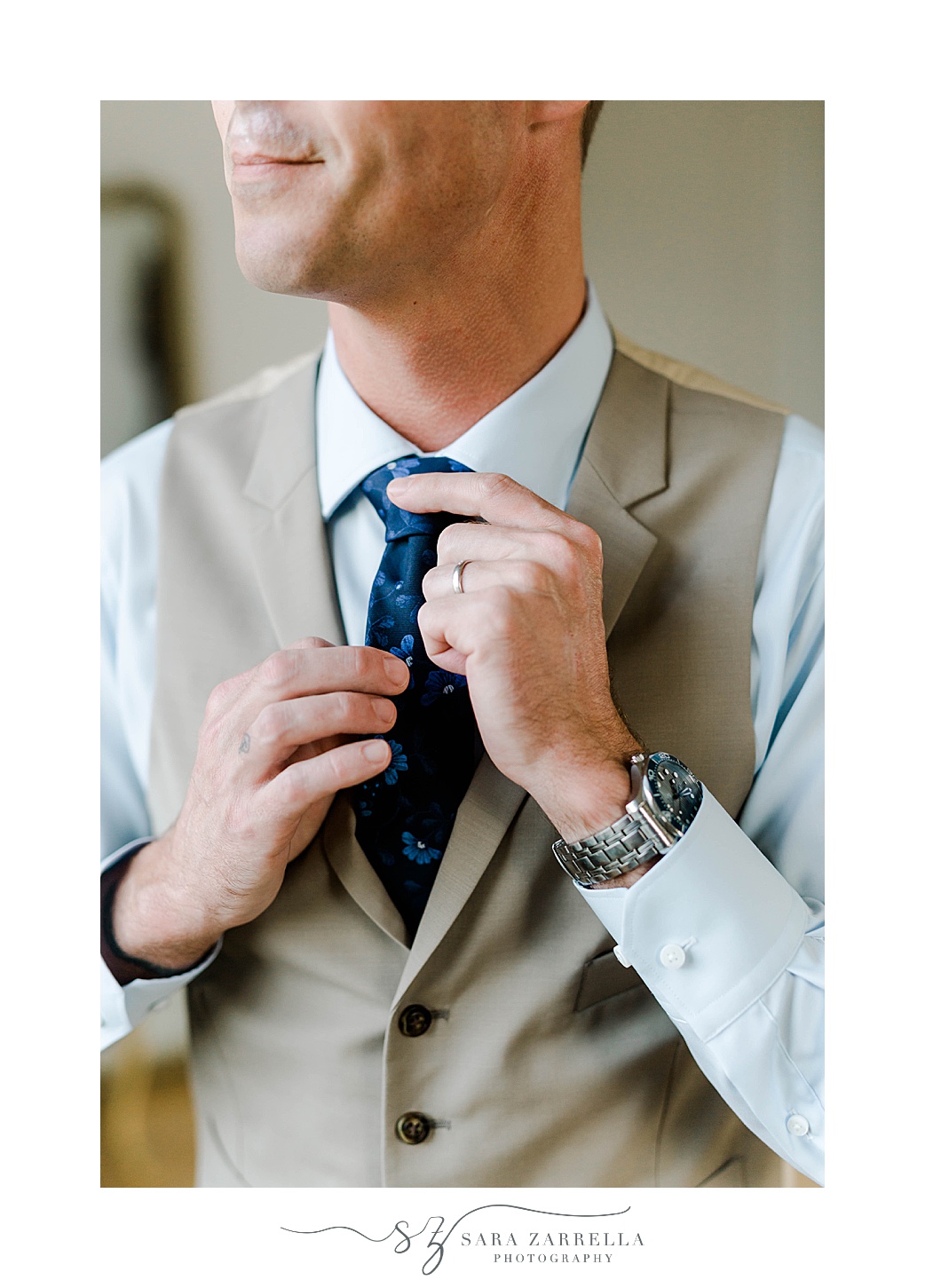 groom adjusts navy tie with khaki vest