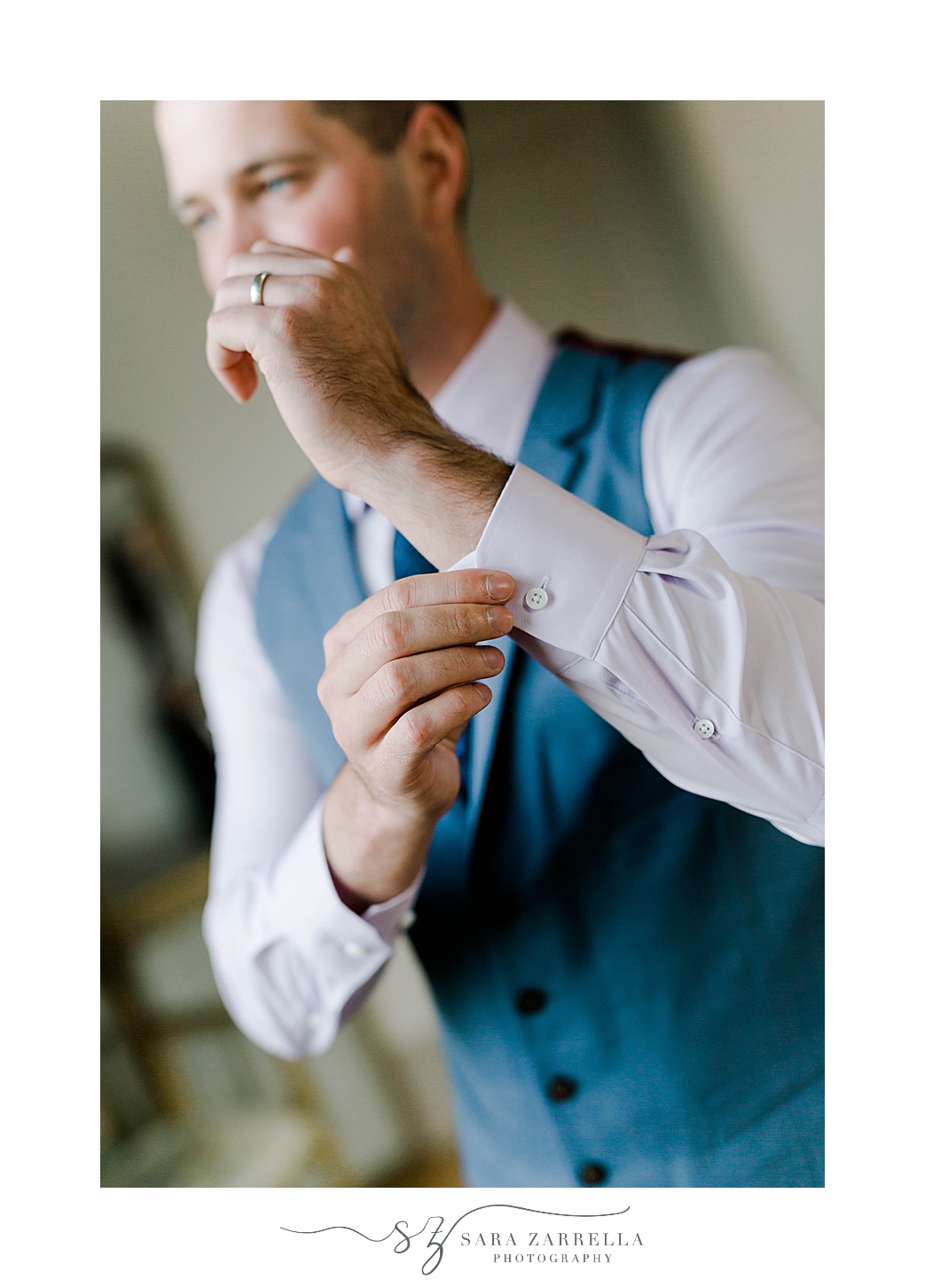 groom adjusts cufflinks in blue vest