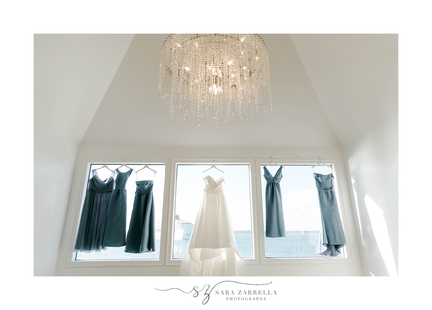 wedding dress hangs in window with blue bridesmaid gowns 