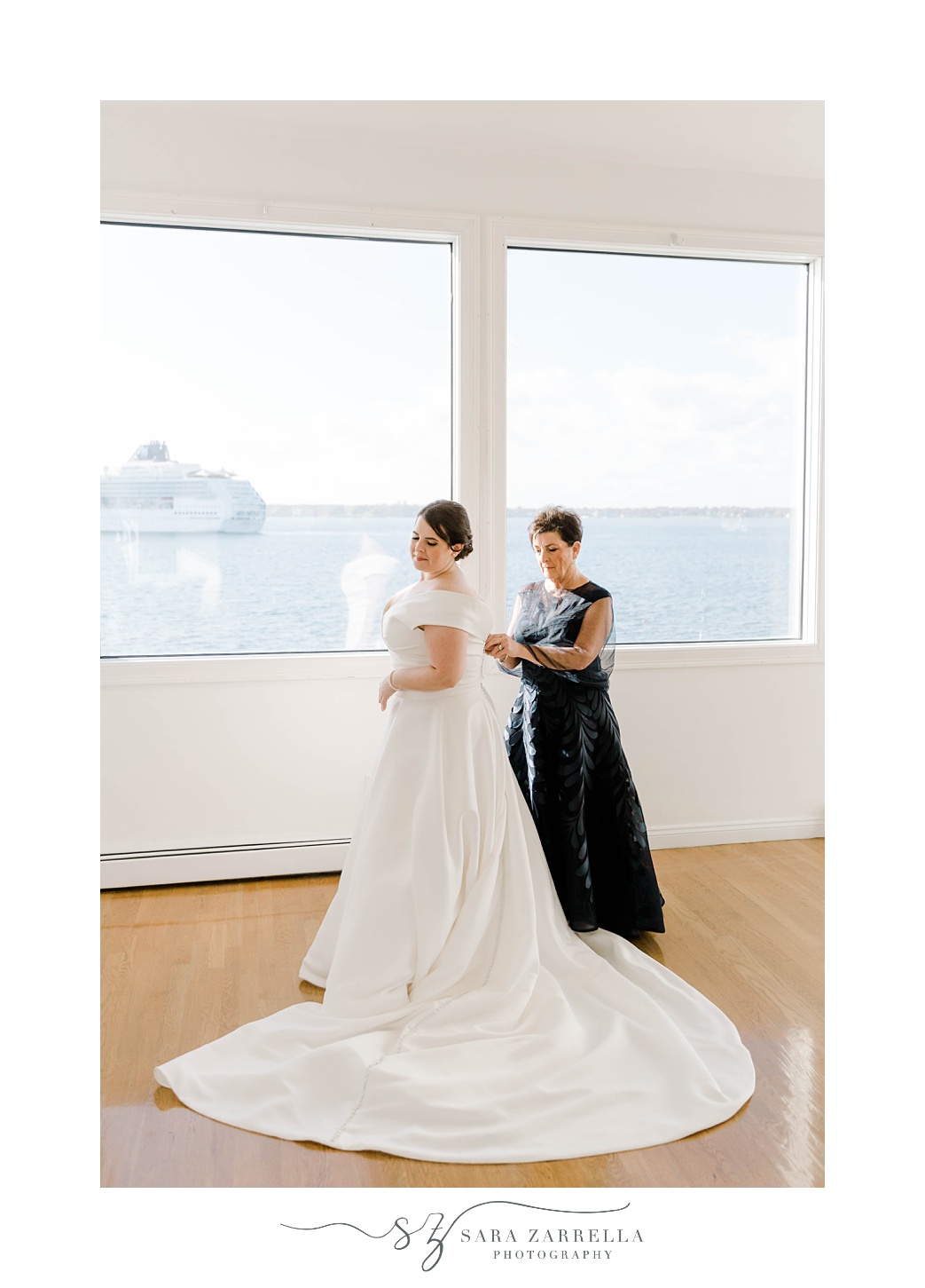 mother in navy gown helps bride into wedding dress by window in suite at Belle Mer