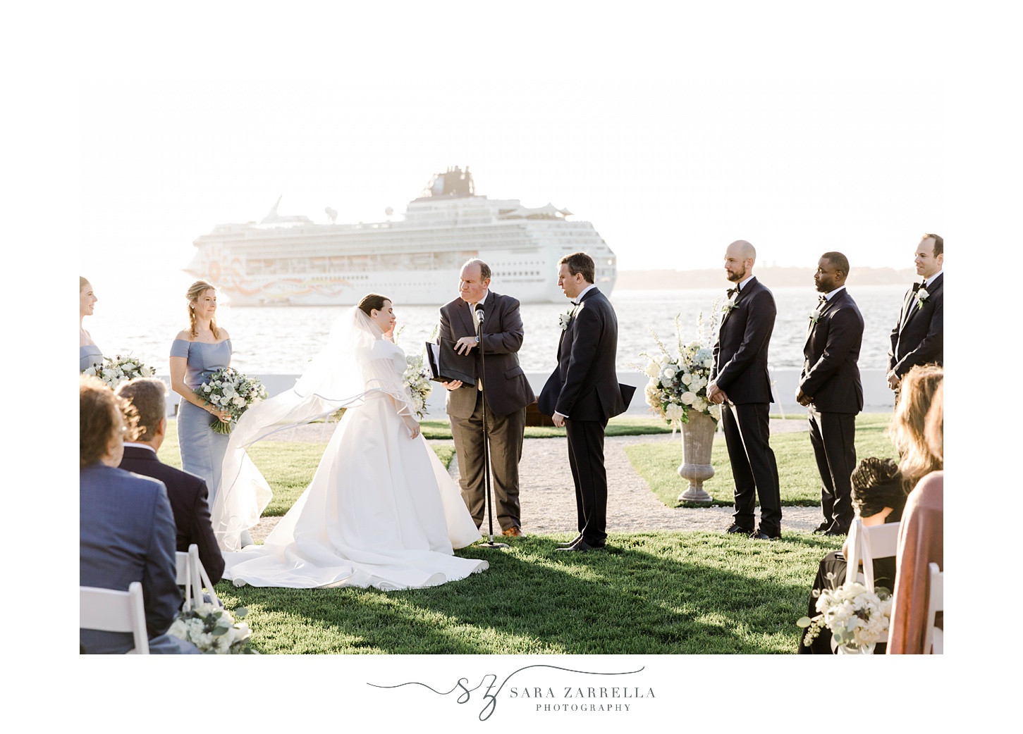 bride and groom stand together during ceremony at Belle Mer with cruise ship behind them 