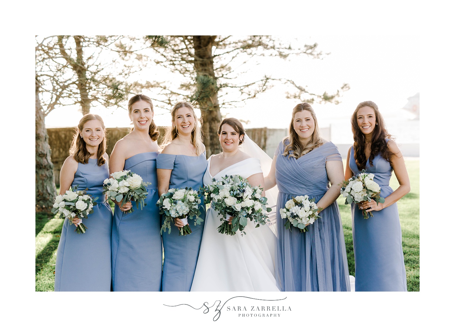 bride smiles with bridesmaids in light blue gowns with blue and white floral bouquets 
