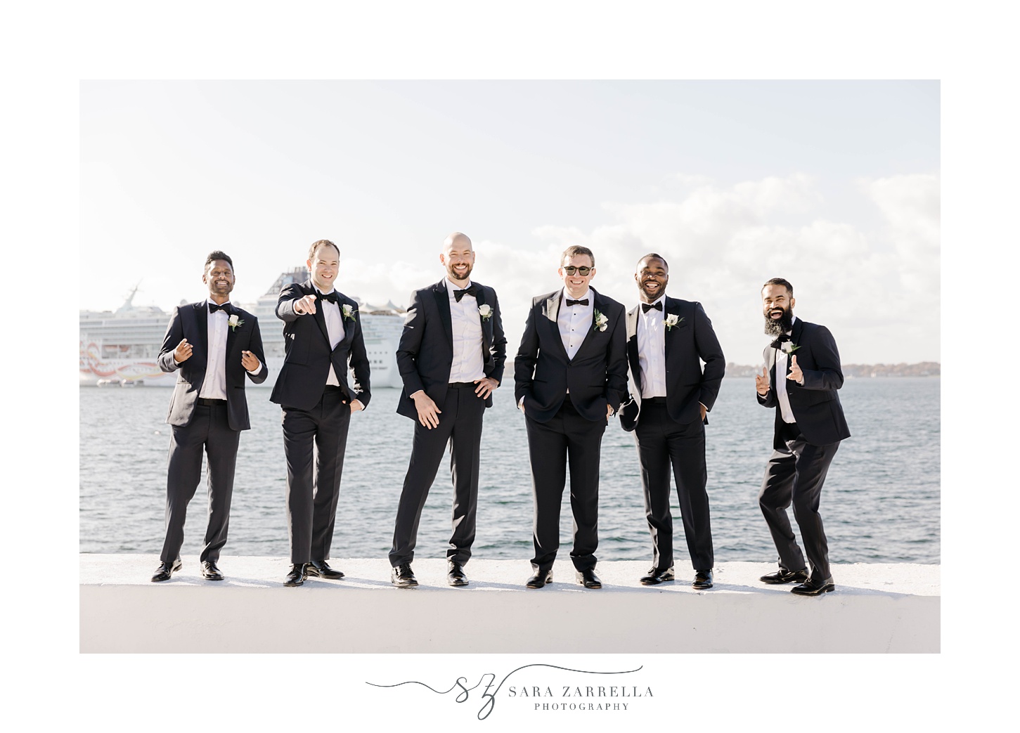 groomsmen laugh standing on wall at Belle Mer in blue suit jackets 