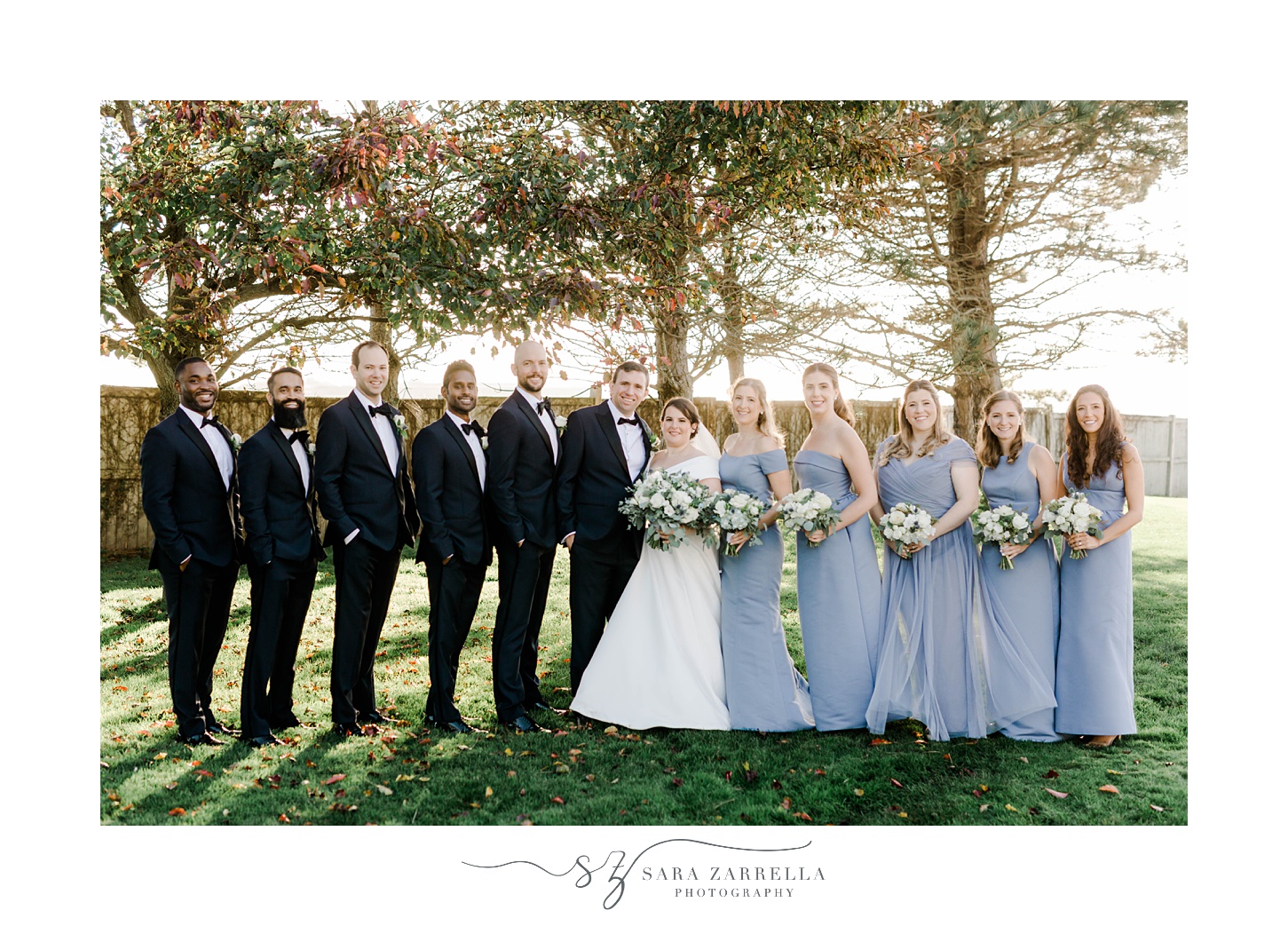 bride and groom stand with wedding party in blue attire at Belle Mer