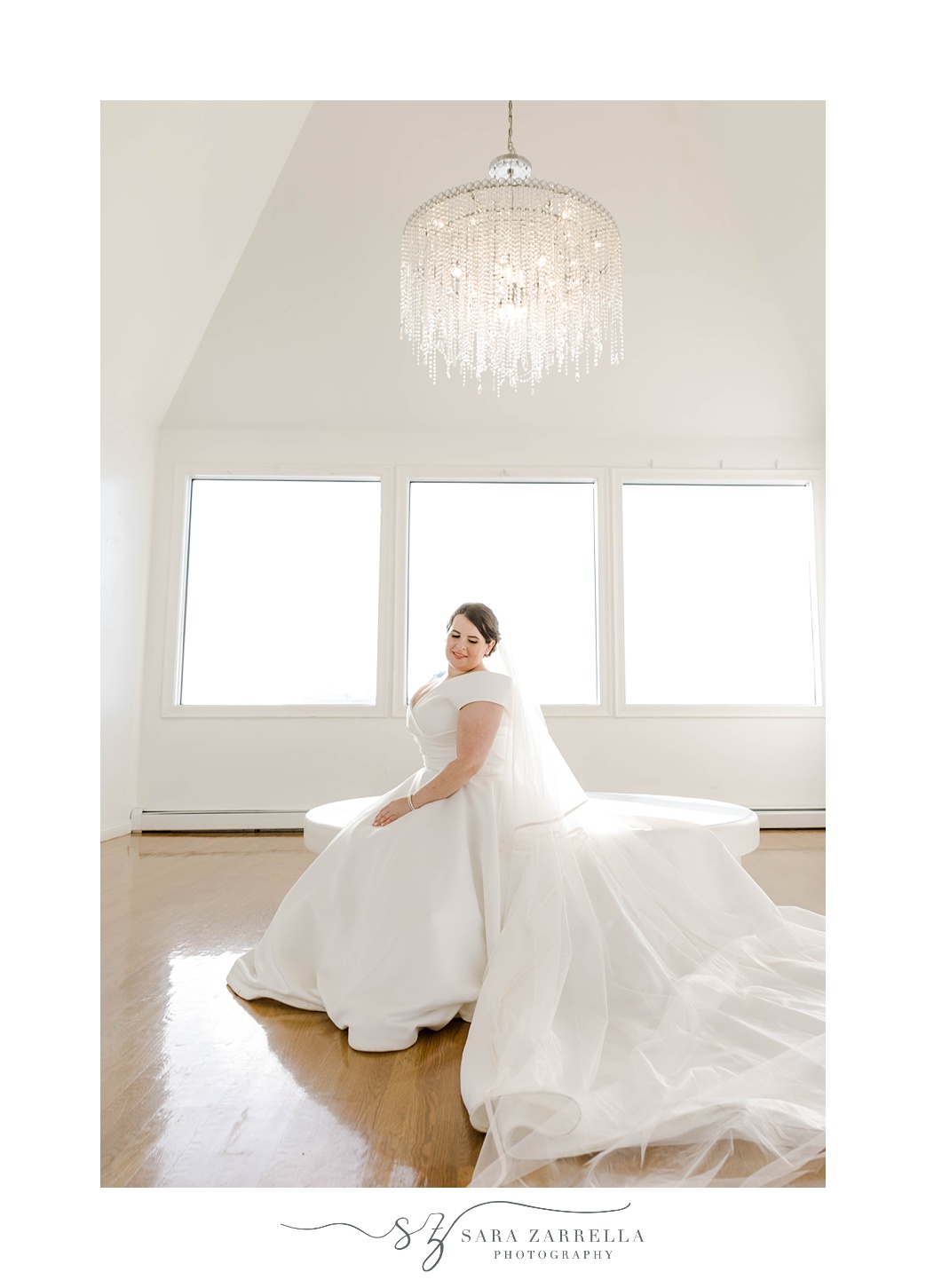 bride sits on white couch with veil draped behind her inside Belle Mer