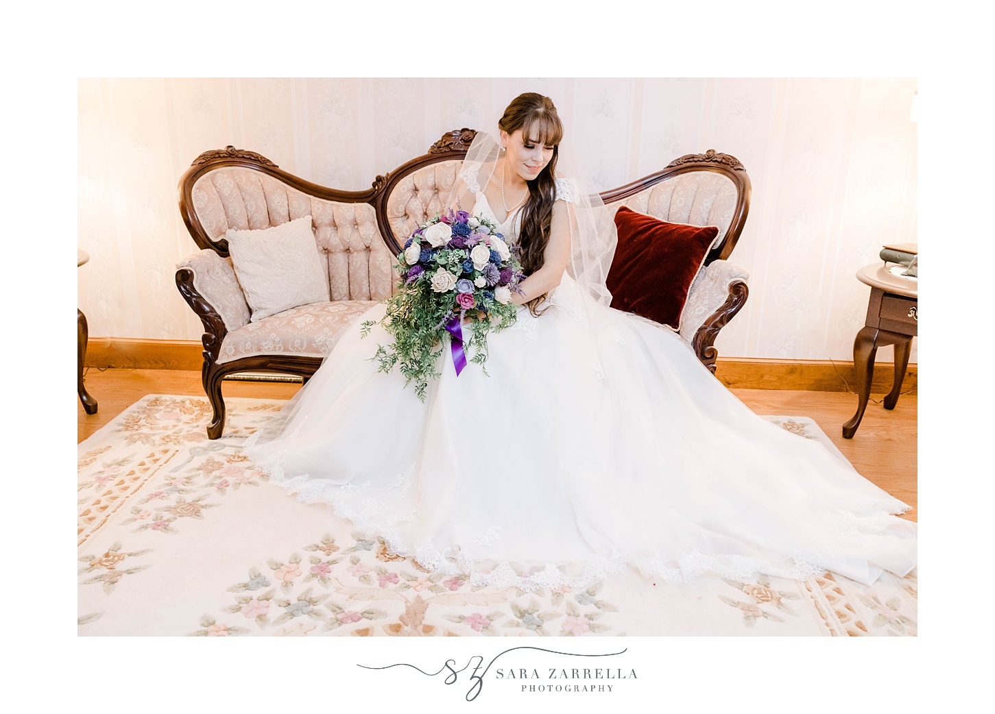 bride sits on antique couch looking at skirt of wedding gown 