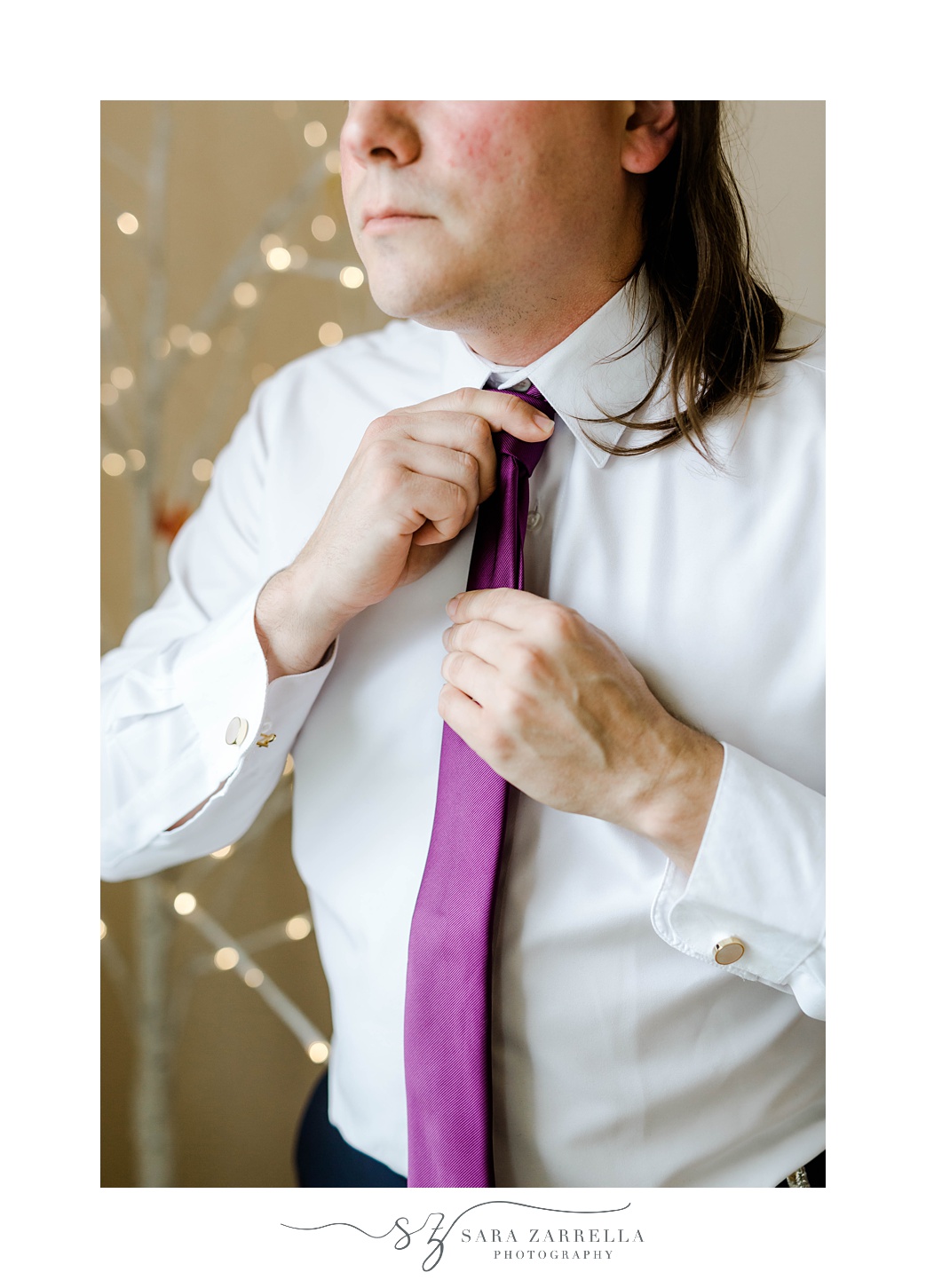 groom adjusts purple tie while preparing for wedding 
