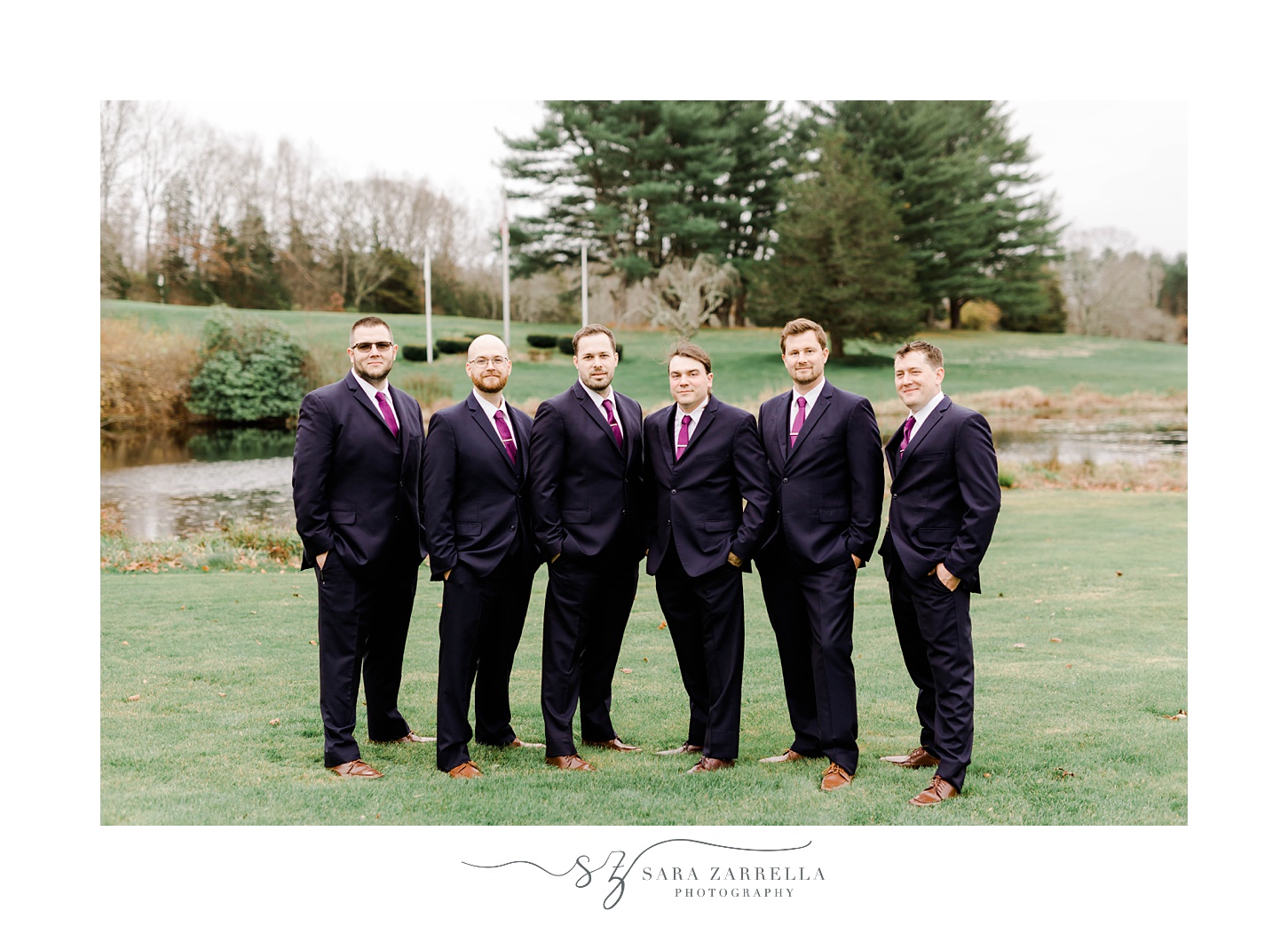 groom stands with groomsmen in black suits with purple ties 