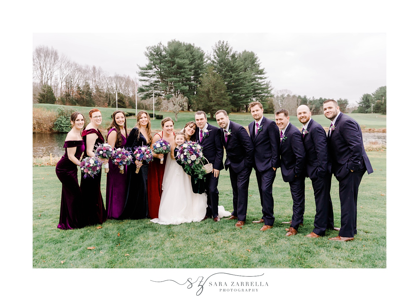 bride and groom stand together with wedding party in black and jewel-tone outfits