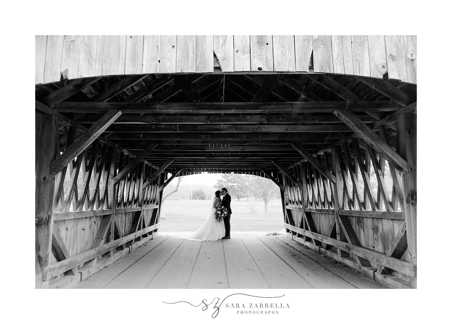 newlyweds kiss under wooden covered bridge at Foster Country Club