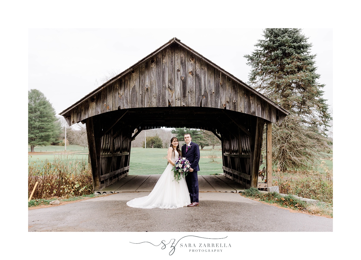 bride and groom hug by wooden covered bridge in Rhode Island 