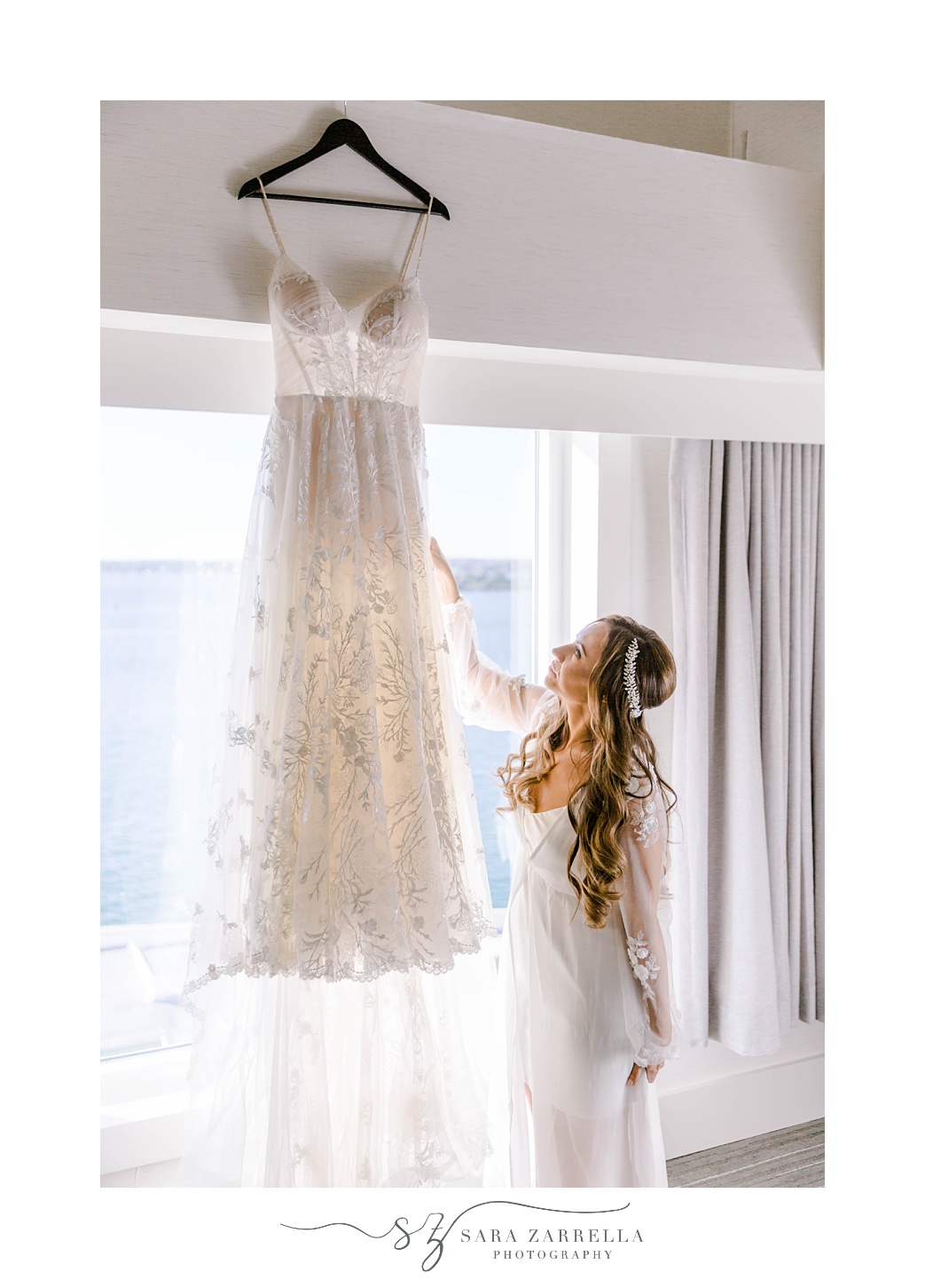 bride looks up at wedding gown hanging in window at Newport Harbor Island Resort