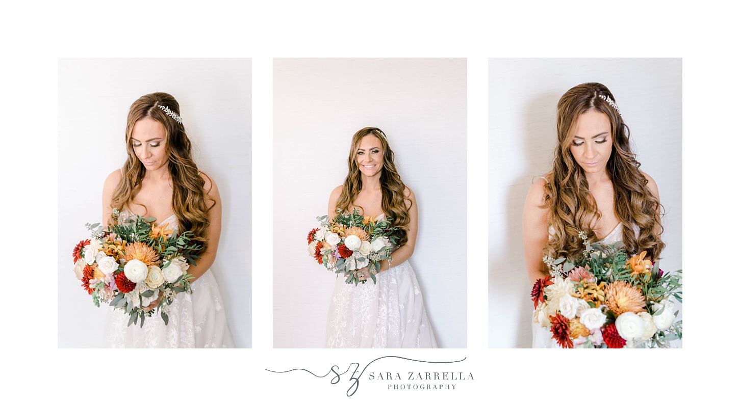 bride stands by wall holding bouquet of red, white and orange flowers